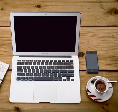 Picture of a desk with a laptop, a phone, and a cup of coffee.